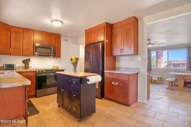 kitchen with ceiling fan, light stone counters, visible vents, appliances with stainless steel finishes, and brown cabinets