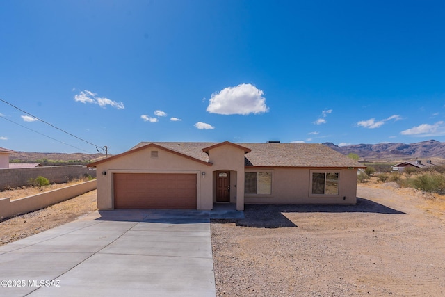 ranch-style home featuring stucco siding, a shingled roof, a mountain view, a garage, and driveway