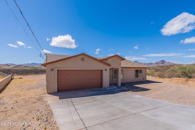 ranch-style house featuring an attached garage, a mountain view, concrete driveway, and stucco siding