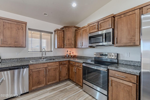 kitchen with brown cabinets, dark countertops, lofted ceiling, appliances with stainless steel finishes, and a sink