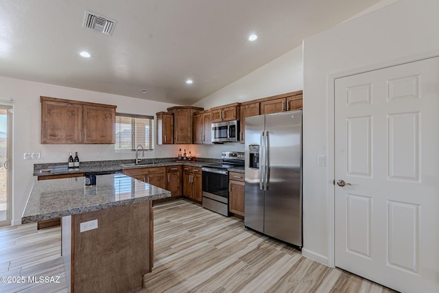 kitchen featuring light wood finished floors, visible vents, appliances with stainless steel finishes, a sink, and dark stone counters