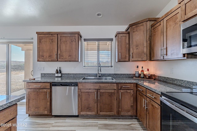 kitchen with appliances with stainless steel finishes, dark stone counters, a healthy amount of sunlight, and a sink