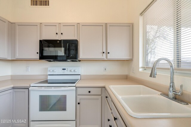 kitchen featuring visible vents, black microwave, light countertops, white electric range, and a sink