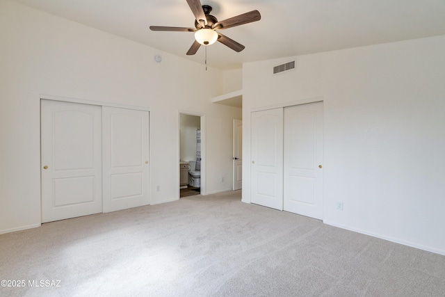 unfurnished bedroom featuring visible vents, vaulted ceiling, light colored carpet, two closets, and connected bathroom