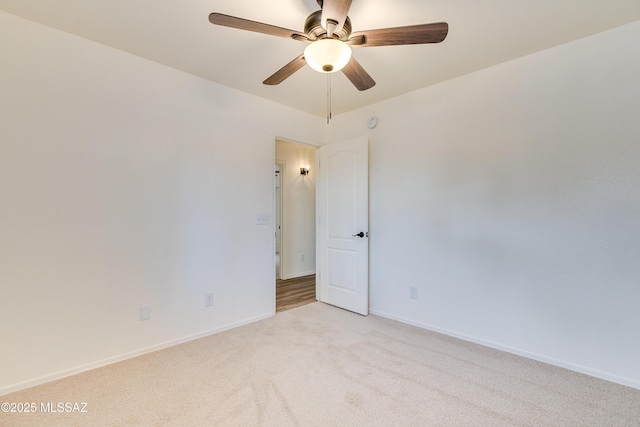 spare room featuring light colored carpet, a ceiling fan, and baseboards