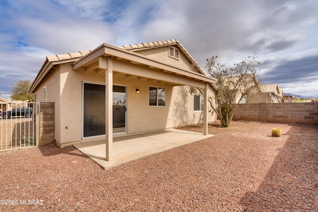 rear view of house with a tiled roof, stucco siding, a patio, and fence