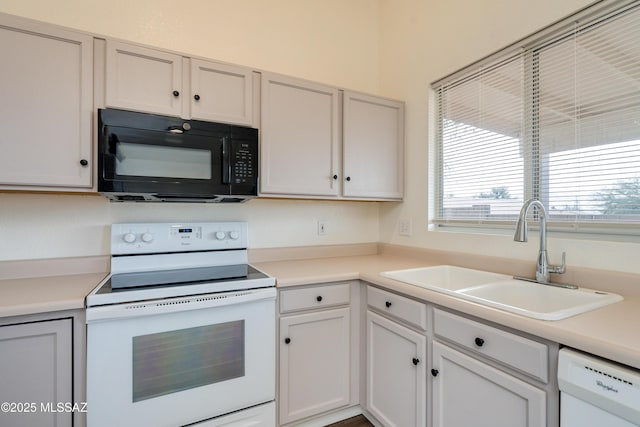 kitchen featuring white appliances, white cabinetry, light countertops, and a sink