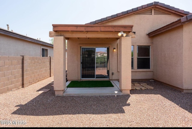 view of exterior entry with a tiled roof, fence, a patio, and stucco siding