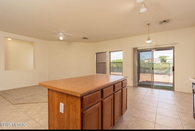 kitchen with brown cabinets, visible vents, hanging light fixtures, open floor plan, and a kitchen island