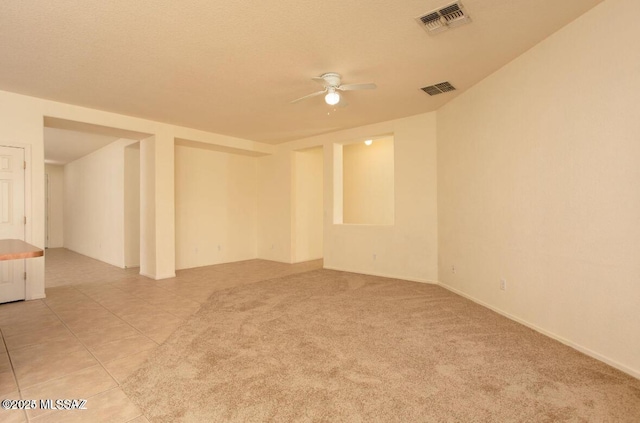 spare room with ceiling fan, light carpet, light tile patterned flooring, and visible vents