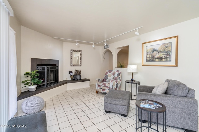 living area featuring light tile patterned floors, arched walkways, and a tiled fireplace