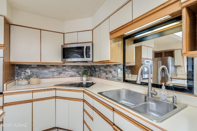 kitchen with stainless steel appliances, light countertops, backsplash, white cabinetry, and a sink