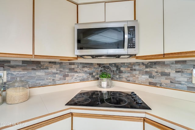 kitchen with black electric stovetop, white cabinetry, light countertops, backsplash, and stainless steel microwave