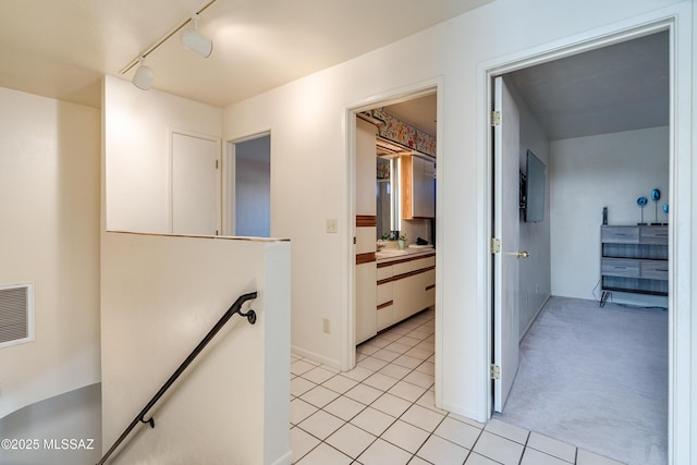 hall featuring visible vents, light colored carpet, an upstairs landing, track lighting, and light tile patterned flooring