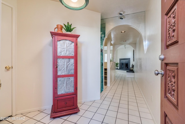 hall with arched walkways, light tile patterned flooring, and baseboards