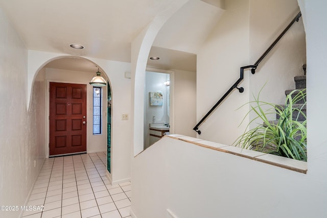 entryway with arched walkways, stairway, recessed lighting, and light tile patterned floors