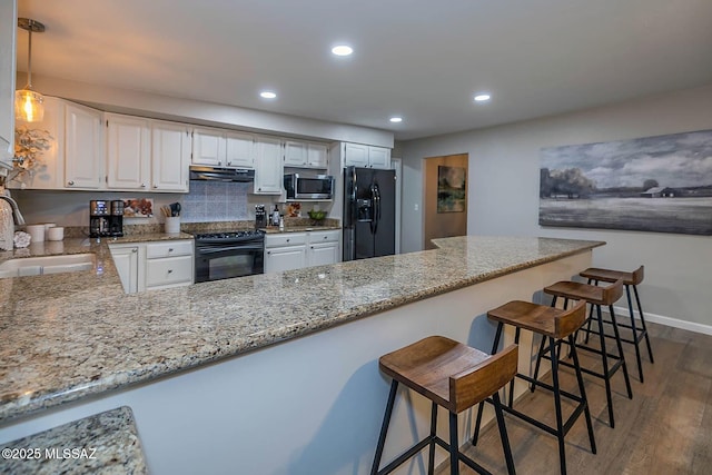 kitchen featuring black appliances, under cabinet range hood, light stone counters, and a sink