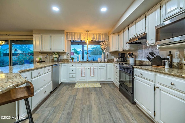 kitchen with light wood-style flooring, appliances with stainless steel finishes, white cabinets, light stone countertops, and under cabinet range hood