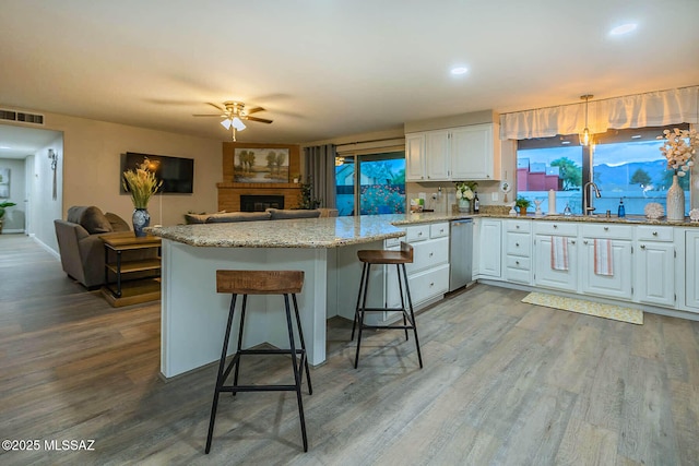 kitchen featuring wood finished floors, visible vents, a ceiling fan, white cabinets, and light stone countertops