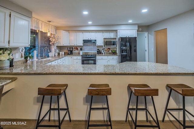 kitchen with recessed lighting, a peninsula, a sink, light stone countertops, and black appliances