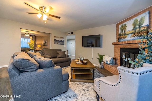 living room with baseboards, visible vents, ceiling fan, wood finished floors, and a brick fireplace