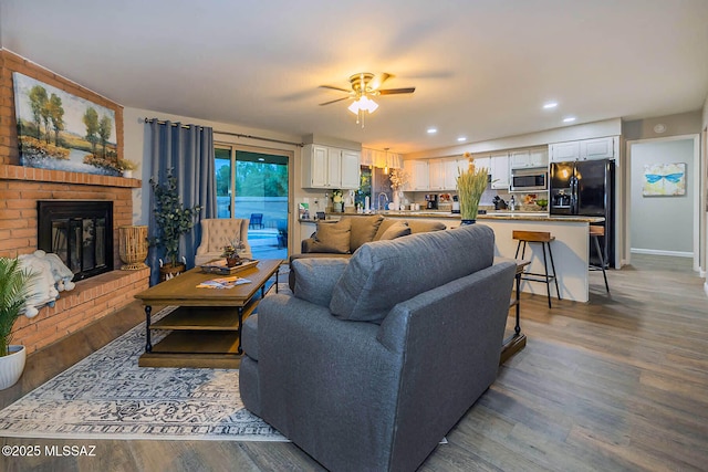 living area featuring baseboards, ceiling fan, wood finished floors, a fireplace, and recessed lighting