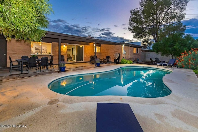 pool at dusk with a patio area, fence, and a fenced in pool