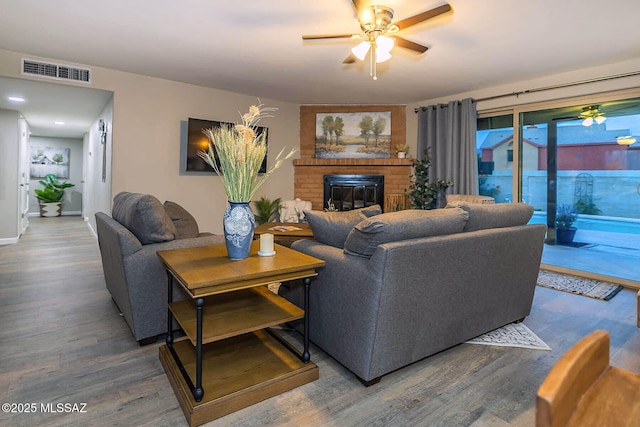 living area with a fireplace, visible vents, a ceiling fan, and wood finished floors