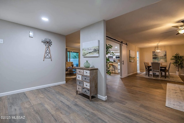 corridor with a barn door, wood finished floors, and baseboards