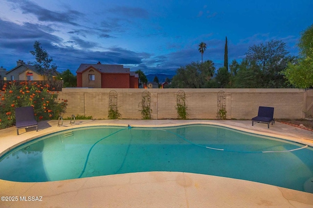 pool at dusk featuring a fenced in pool, a fenced backyard, and a patio