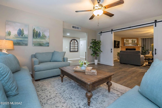 living area featuring a ceiling fan, a barn door, visible vents, and wood finished floors