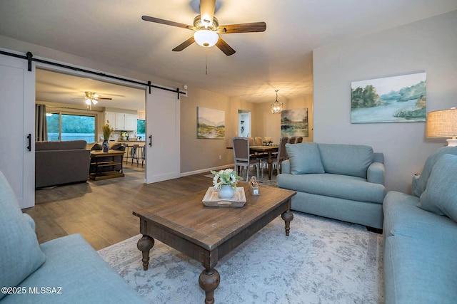 living room featuring wood finished floors, ceiling fan, baseboards, and a barn door