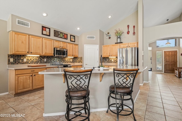 kitchen with arched walkways, light countertops, visible vents, appliances with stainless steel finishes, and a kitchen breakfast bar