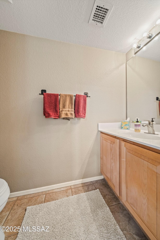 bathroom with a textured ceiling, vanity, visible vents, and baseboards