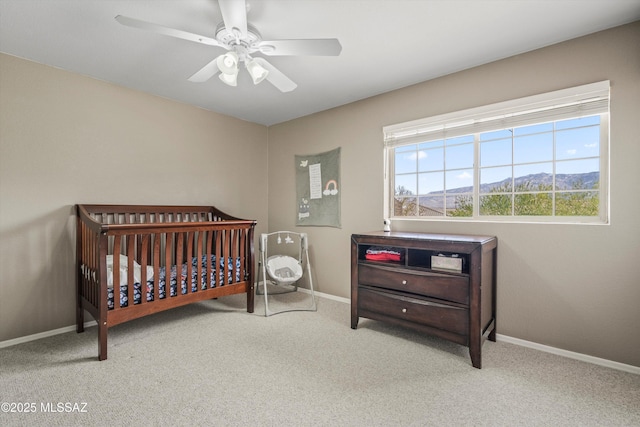 carpeted bedroom with ceiling fan, a crib, and baseboards