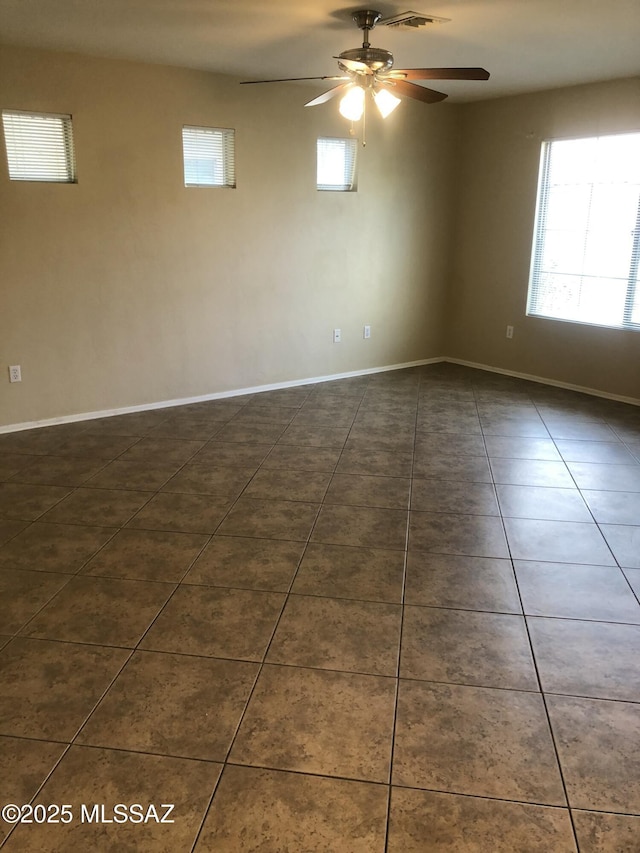 empty room with visible vents, a healthy amount of sunlight, dark tile patterned floors, and baseboards