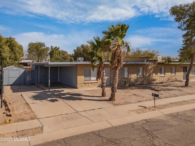 view of front of property with an outbuilding, brick siding, a storage unit, concrete driveway, and a carport