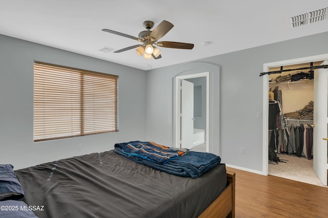 bedroom with a closet, visible vents, ensuite bathroom, and wood finished floors