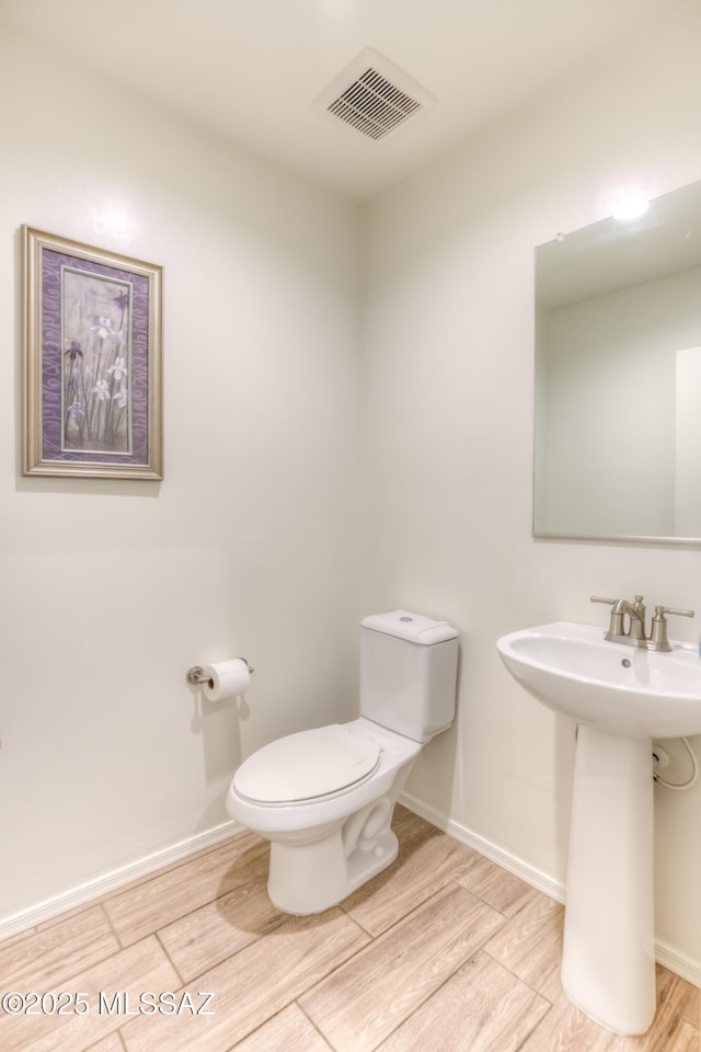 half bath with baseboards, visible vents, toilet, wood finished floors, and a sink