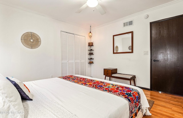 bedroom featuring crown molding, a closet, visible vents, light wood-style flooring, and ceiling fan