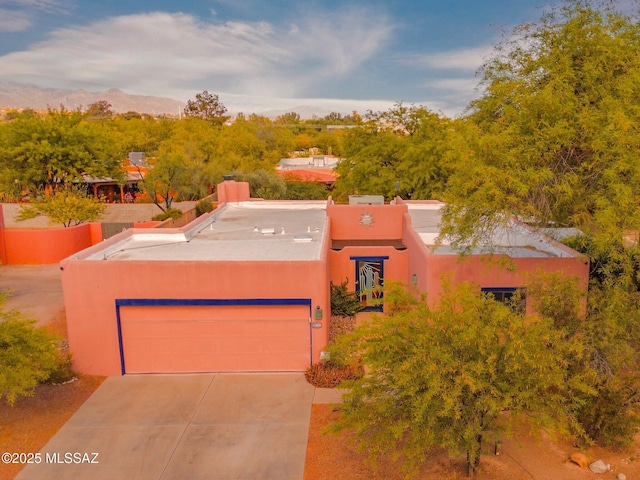 pueblo-style home featuring an attached garage, concrete driveway, and stucco siding