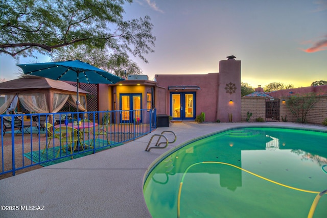 pool at dusk featuring a fenced in pool, french doors, a patio area, and fence