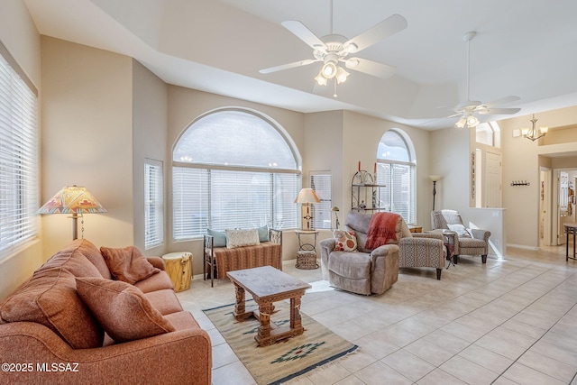 living room with a high ceiling, light tile patterned flooring, ceiling fan with notable chandelier, and baseboards