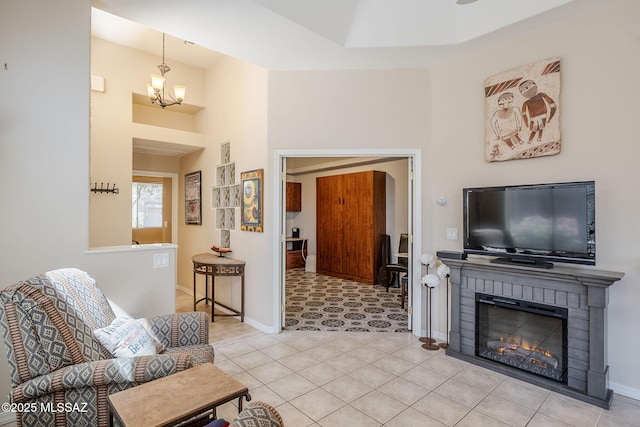 living area with a brick fireplace, baseboards, a chandelier, light tile patterned floors, and a high ceiling