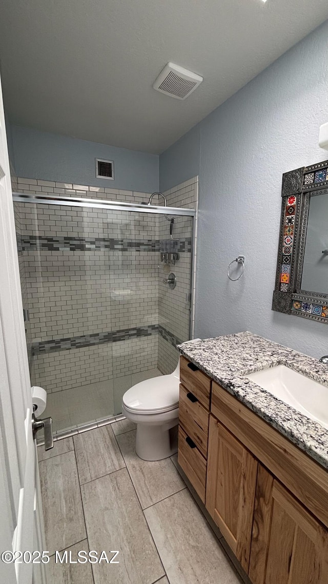 bathroom featuring visible vents, a stall shower, toilet, and vanity