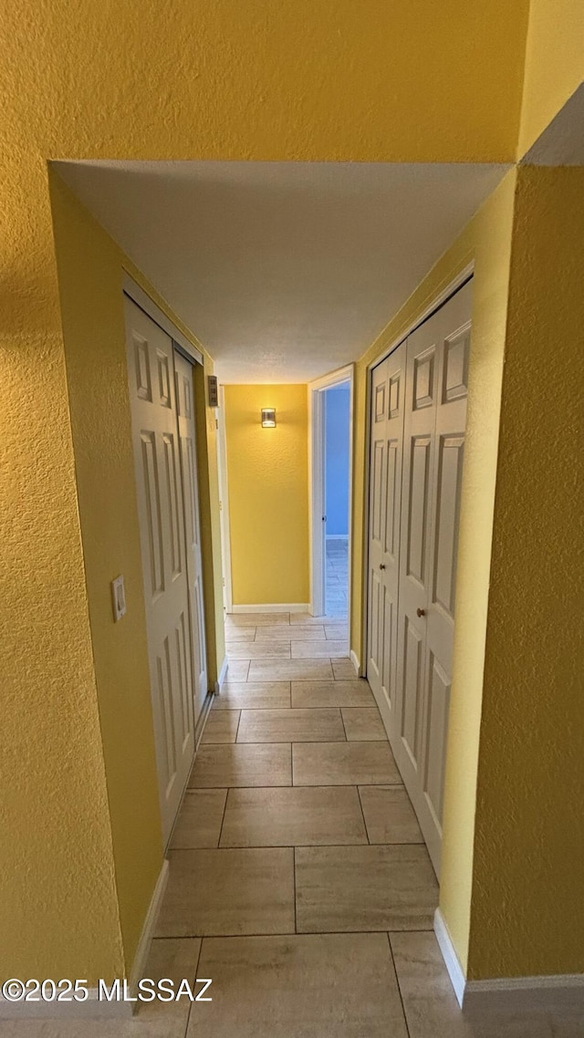 hallway featuring baseboards and a textured wall