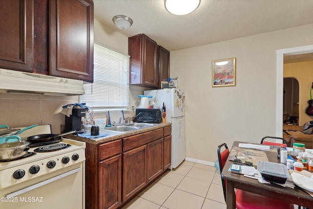 kitchen featuring light tile patterned floors, white appliances, baseboards, under cabinet range hood, and a sink