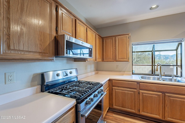 kitchen featuring light countertops, appliances with stainless steel finishes, a sink, light wood-type flooring, and brown cabinetry