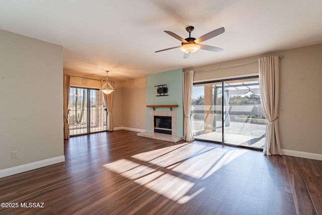 unfurnished living room with dark wood-style flooring, a tiled fireplace, ceiling fan, and a healthy amount of sunlight