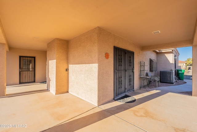view of exterior entry featuring stucco siding, central AC, and a patio
